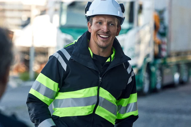 Cran truck driver driver wearing a yellow/black high-visibility jacket and work trousers from Fristads.
